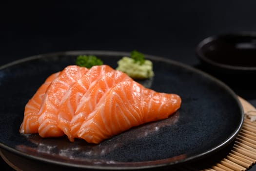 Closeup fresh salmon sachimi with soy sauce and wasabi on black plate.
