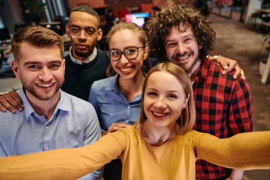 A diverse group of business professionals take a break from their tasks in a modern startup office to capture a creative selfie, showcasing teamwork and a vibrant workplace culture.