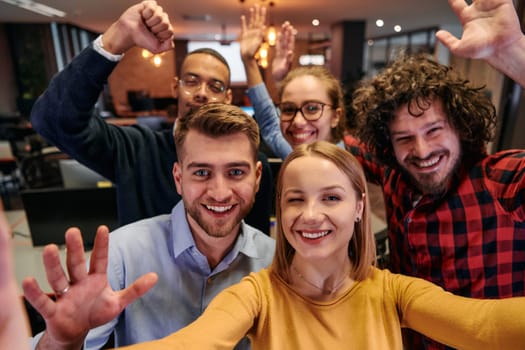 A diverse group of business professionals take a break from their tasks in a modern startup office to capture a creative selfie, showcasing teamwork and a vibrant workplace culture.