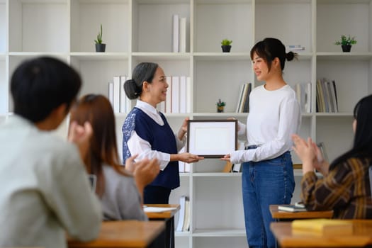 Middle age female teacher handing over certificates to best female student.