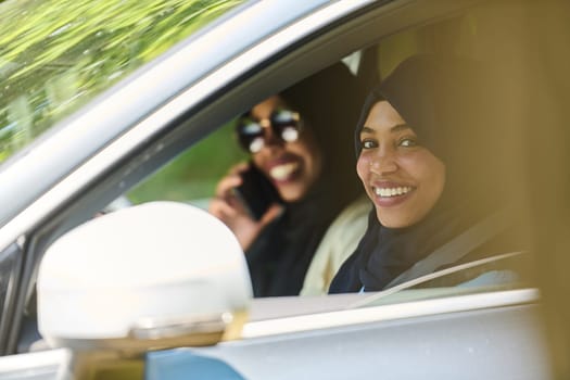 Two Muslim women wearing hijab converse on a smartphone while traveling together in a car through the.