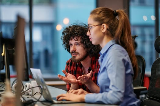 Business colleagues, a man and a woman, engage in discussing business strategies while attentively gazing at a computer monitor, epitomizing collaboration and innovation.