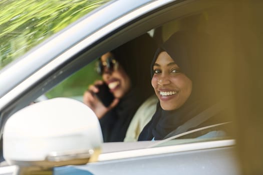 Two Muslim women wearing hijab converse on a smartphone while traveling together in a car through the.