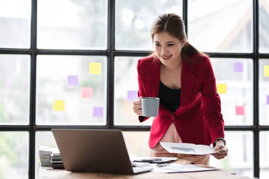 beautiful business woman Focused on paperwork using laptop and calculator to calculate turnover in modern office.