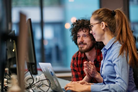 Business colleagues, a man and a woman, engage in discussing business strategies while attentively gazing at a computer monitor, epitomizing collaboration and innovation.