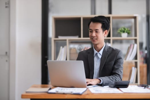 Young Asian man working on laptop in modern office analyze accounting, report real estate investment information..