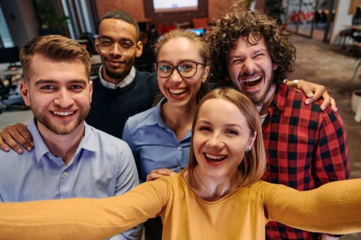 A diverse group of business professionals take a break from their tasks in a modern startup office to capture a creative selfie, showcasing teamwork and a vibrant workplace culture.