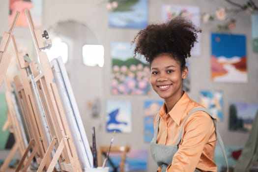 A young black artist paints acrylic paints on canvas with determination in her painting studio.