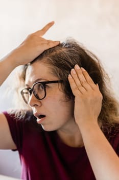 Woman Looking for Gray Hair in the Mirror. Young woman scared of premature aging signs.