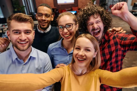 A diverse group of business professionals take a break from their tasks in a modern startup office to capture a creative selfie, showcasing teamwork and a vibrant workplace culture.