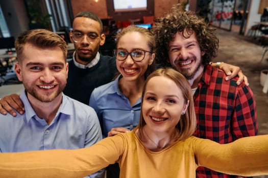 A diverse group of business professionals take a break from their tasks in a modern startup office to capture a creative selfie, showcasing teamwork and a vibrant workplace culture.