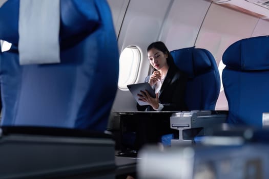 A woman is sitting in an airplane seat with a laptop open in front of her. She is wearing a suit and she is working on her laptop. Concept of productivity and focus