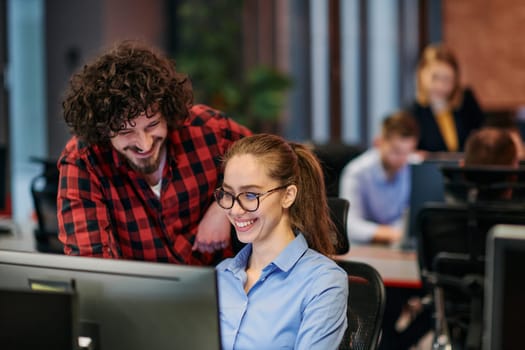 Business colleagues, a man and a woman, engage in discussing business strategies while attentively gazing at a computer monitor, epitomizing collaboration and innovation.