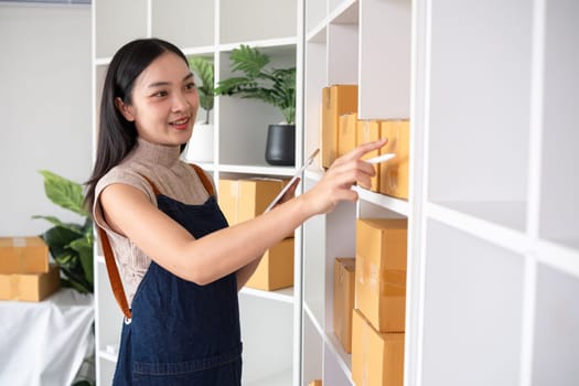 A small SME business owner checks an order and writes shipping information on a cardboard box in his home office to prepare for delivery..