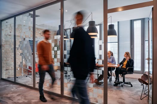 In the dynamic hustle and bustle of a business environment, a group of young business professionals walk down the corridor next to their office, while their colleagues collaborate inside, symbolizing teamwork and productivity.