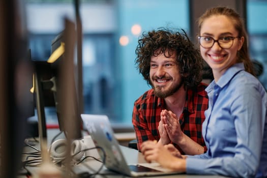 Business colleagues, a man and a woman, engage in discussing business strategies while attentively gazing at a computer monitor, epitomizing collaboration and innovation.