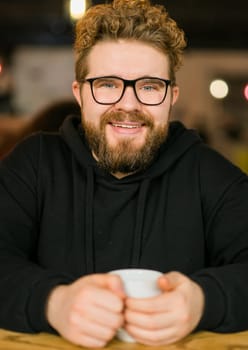 Close up portrait of young handsome freelance man wearing stylish eyeglasses on cafe. Happy confident student looking at camera, education and online work concept. Millennial generation and Gen Y