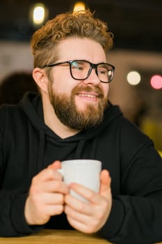 Bearded curly man smiling confident drinking coffee in restaurant or coffee shop. Millennial generation and Gen Y.