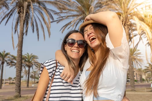 Happy friends laughing and holding each other in the beach. Cheerful girls embracing each other. High quality photo