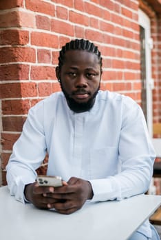 African american man checks cell phone in the street cafe in summer day. Millennial generation and gen z people. Social networks and dating app