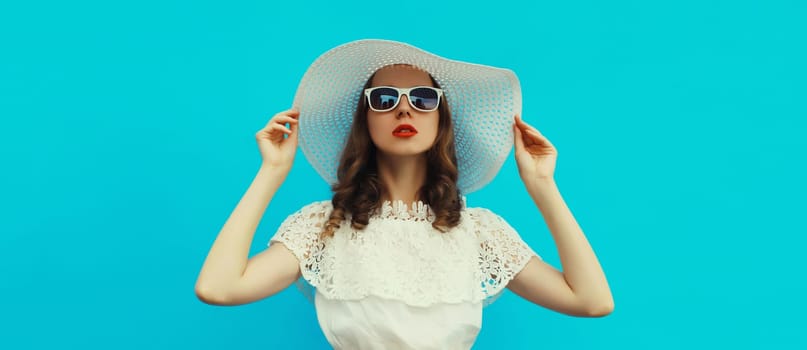 Portrait of beautiful caucasian young woman model posing wearing white summer straw hat on blue studio background