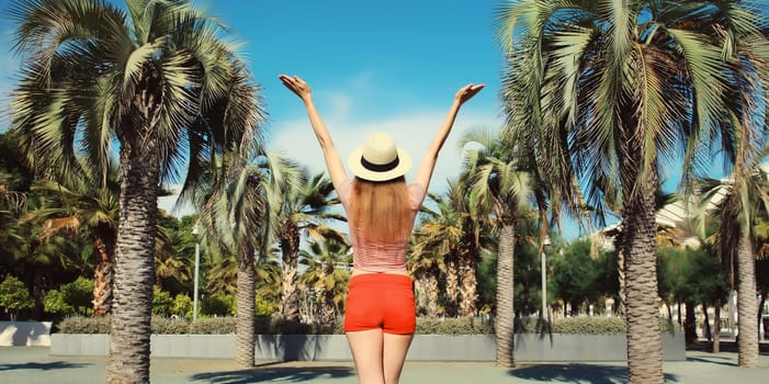 Summer vacation, happy cheerful young woman raising her hands up against a palm trees background