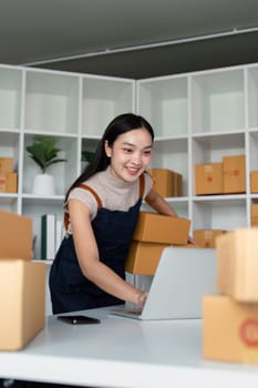 Startup small business entrepreneur of freelance Asian woman using laptop and box to receive and review order online to prepare to pack sell to customer, online business ideas.