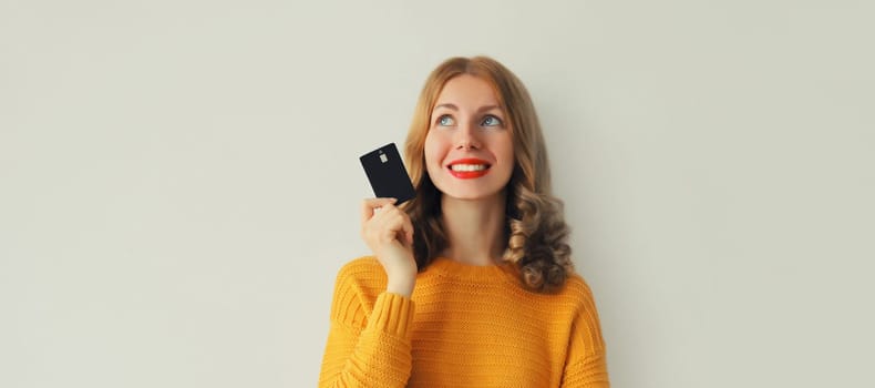 Portrait of happy smiling young woman holding plastic credit bank card and looking up on studio background