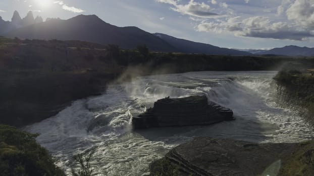 Slow-mo video captures a majestic waterfall at dusk with Torres del Paine silhouetted against the setting sun.