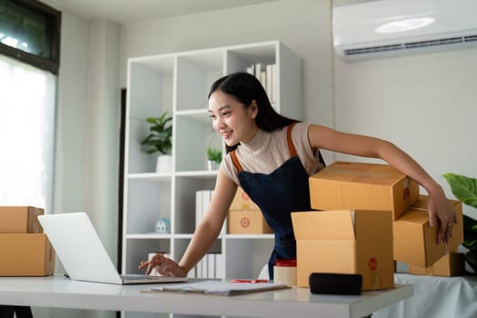 Startup small business entrepreneur of freelance Asian woman using laptop and box to receive and review order online to prepare to pack sell to customer, online business ideas.