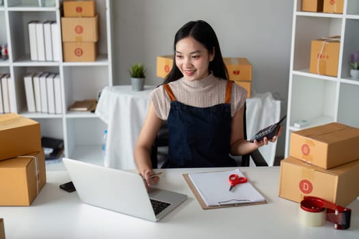 Startup small business entrepreneur of freelance Asian woman using laptop and box to receive and review order online to prepare to pack sell to customer, online business ideas.