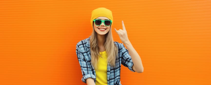 Summer portrait of happy cheerful stylish young woman in colorful clothes, yellow hat posing on orange background on city street