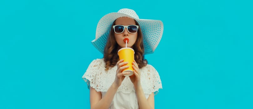 Summer portrait of beautiful caucasian young woman with cup of coffee or fresh juice wearing white straw hat on studio blue background