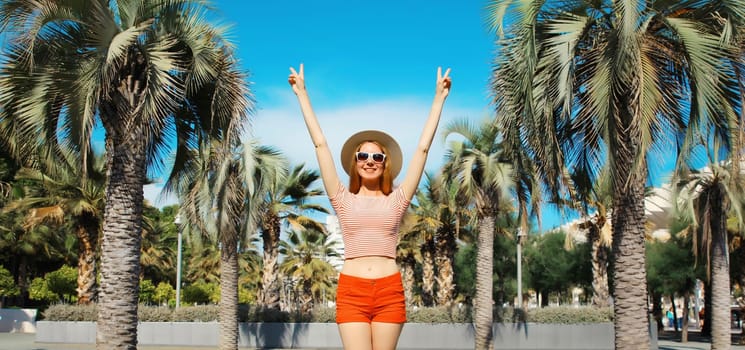 Summer vacation, happy cheerful young woman raising her hands up against a palm trees background