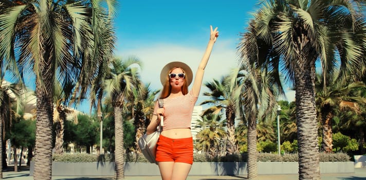 Cheerful young woman in summer park wearing backpack against a palm tree background