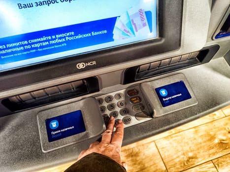 Kirov, Russia - April 28, 2024: Person Withdrawing Cash From ATM in Russia. Hand pressing button on an ATM with a Russian language screen