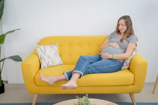 Smiling pregnant woman embracing belly in living room with copy space for text. High quality photo