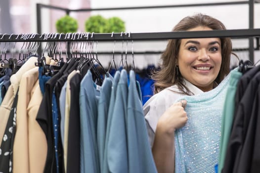 Portrait of a fat woman in a plus size store through hangers with clothes