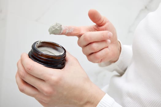 female hand takes a clay face mask from a jar. home spa. close-up