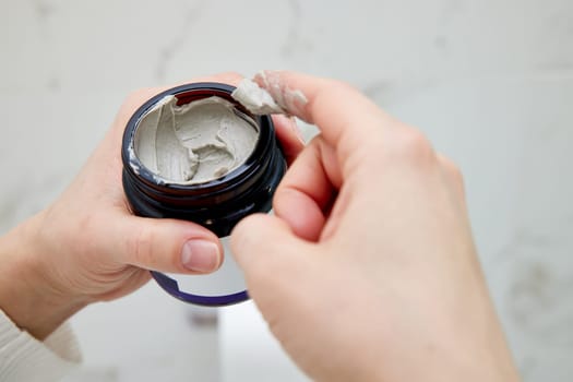 female hand takes a clay face mask from a jar. home spa