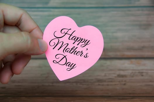 Hand holding Happy Mother's Day text on pink paper. Mother's day concept.