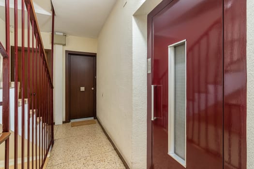 An interior shot of a residential building foyer with a classic red door and terrazzo flooring.