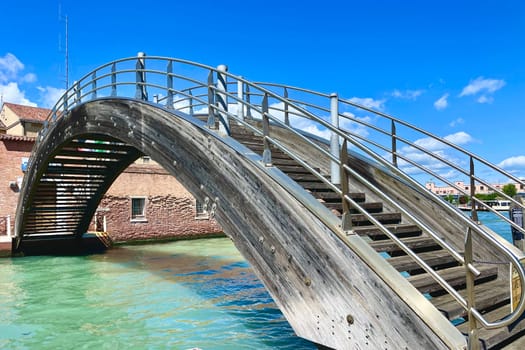 Wooden arched bridge across the strait in Venice under a blue sky. High quality photo
