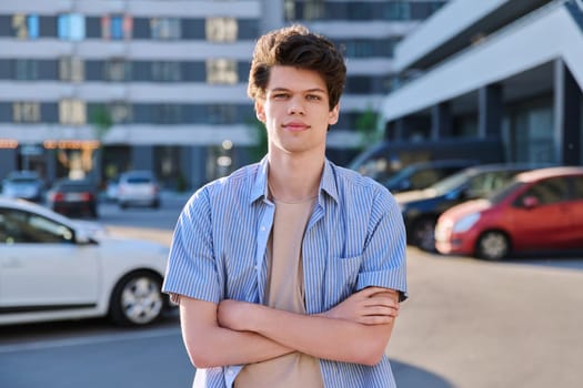 Portrait of confident smiling college student guy, young handsome male with crossed arms looking at camera, urban city outdoor. Education, lifestyle, 19,20 years age youth concept