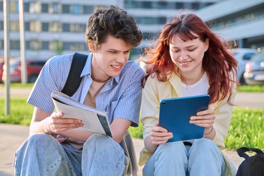 Teenage college students guy and girl talking, using digital tablet, sitting outdoor, urban modern city. Youth 19-20 years old, education, technologies, lifestyle, friendship concept