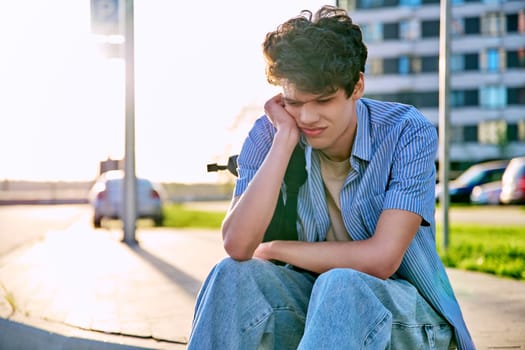 Upset sad unhappy young male sitting outdoor on steps. Guy university college student with backpack sitting, holding head with hands. Problems, difficulties, depression, mental health of young people