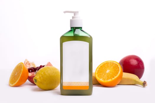 green bottle with dispenser without design next to fruit on a white background.