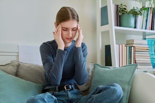 Upset sad lonely young woman sitting on couch at home. Disappointed female 19-20 years old, girl college student in sadness. Depression, stress, mental difficulties, youth concept