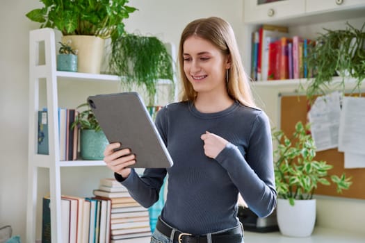 Young teenage female student at home looking talking in web camera of digital tablet. Girl teenager 16,17,18 years old studying remotely, video conference call, e-learning technology education