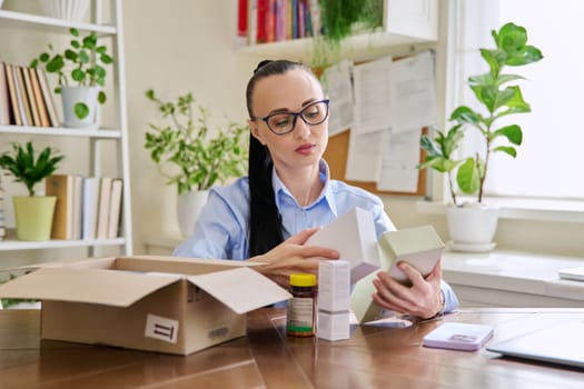 Satisfied female consumer buyer sitting at home unpacking cardboard box with online purchases. Woman unpacking boxes with cosmetics care products vitamins perfumes. Delivery by mail, online store